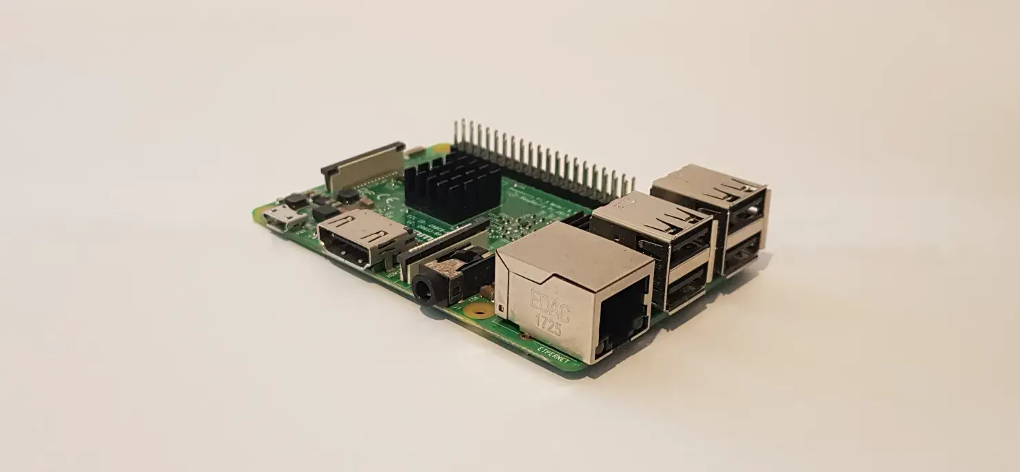 An angled photograph of a Raspberry Pi Model 3 B placed against a white and detail-less backdrop. The device has nothing connected to it, and has a black finned heatsink placed over the CPU.